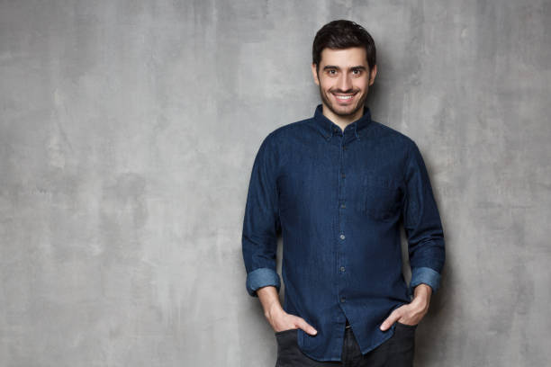 istock Young confident smiling man standing against gray wall with copy space on left side 1164586379