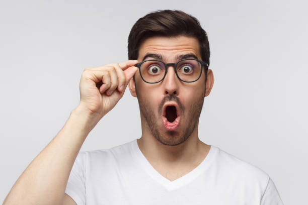 istock Young man shouting, confused with shock content, holding glasses with one hand, isolated on gray background 1164586428