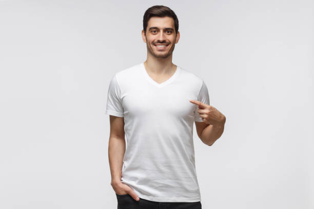 istock Young man pointing with index finger at blank  t-shirt with empty space for your text or image, standing isolated on gray background 1164586521