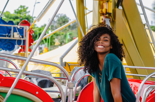 giovane ragazza di colore nero, capelli che ridono in ruota panoramica, seduta godendosi una giornata estiva, ritratto stile di vita - child caribbean black latin american and hispanic ethnicity foto e immagini stock