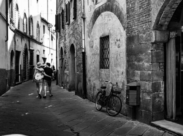 Black and white photographic image of a young Italian couple walk down a street together in Lucca, Italy stock photo