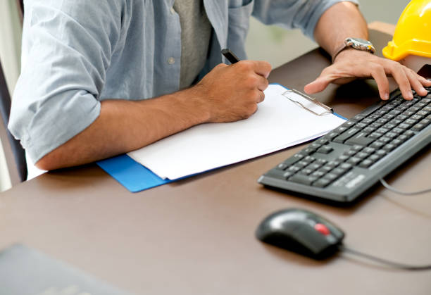 istock Engineer man is writing something on the paper while typing on keyboard of computer with concept of working at home 1164590725