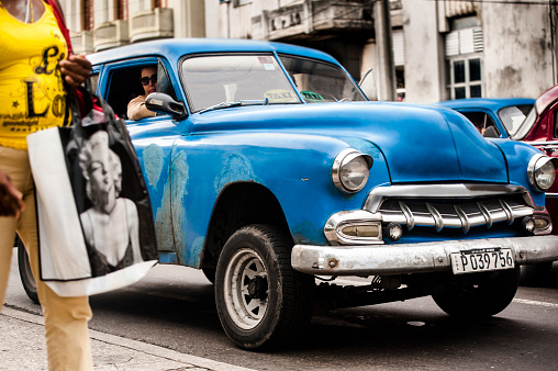 Havana, Cuba - December 12, 2013: A woman carrying a Marilyn Monroe bags walks down a street in Havana, Cuba in front of a vintage car