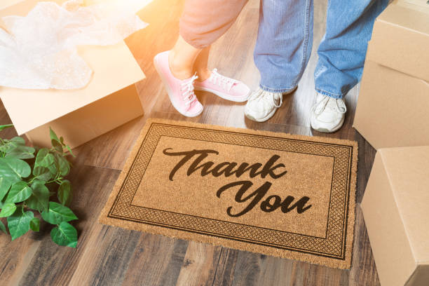 Man and Woman Unpacking Near Thank You Welcome Mat, Moving Boxes and Plant stock photo