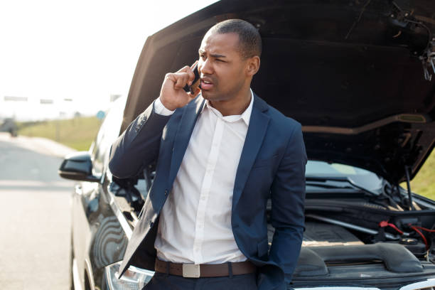 istock Young man leaning on car with opened hood talking on smartphone asking for help concerned 1164612701