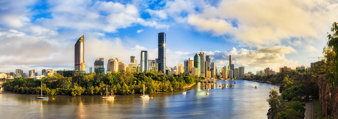 Elevated panorama of Brisbane city CBD surrounded by waters of Brisbane river from Cliffs park in soft morning light after rain.