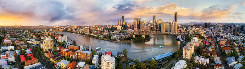 180 degrees aerial panorama around Brisbane city CBD high-rise towers looped by Brisbane river with Story bridge across. Colourful sunrise shining over city streets and houses.