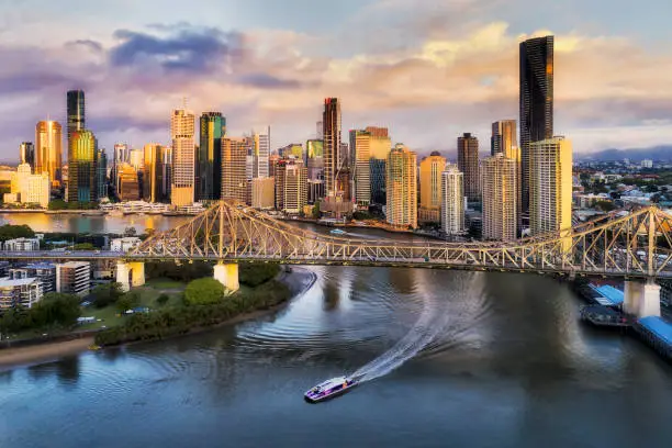 CLose to Story bridge across Brisbane river in front of Brisbane city CBD high-rise business and apartment towers with fast ferry on the water under the bridge.