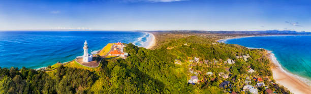 D Byron Bay Lighthouse Close TOp pan Top of headland with Byron Bay lighthouse high above Pacific ocean coast on a sunny day in elevated aerial panorama facing inland over sandy beaches. headland photos stock pictures, royalty-free photos & images