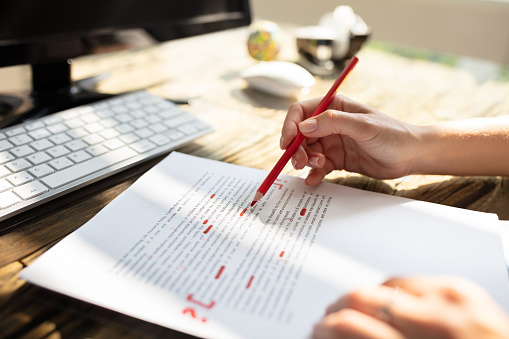 Close-up Of A Person's Hand Marking Error With Red Marker On Document