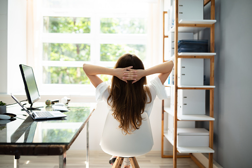 Rear View Of Relaxed Businesswoman With Hands Behind Head Sitting In Office