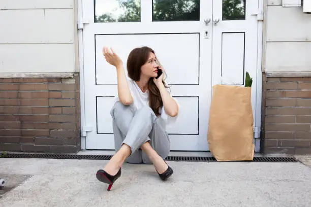 An Afraid Young Woman Sitting Outside The Door Talking On Mobilephone