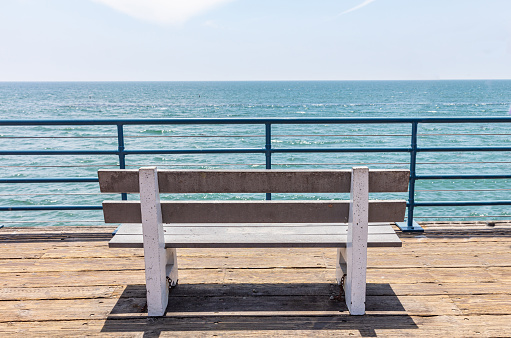 Empty bench with sea view on wooden deck, blue sky and sea background, Santa Monica pier, California