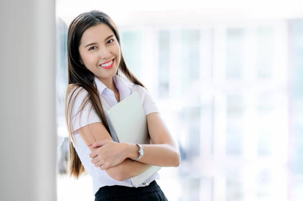 istock Portrait of young student smiling and holding tablet while standing in classroom. 1164651643