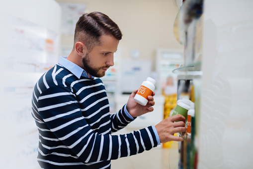 Put it. Attentive male person bowing head while taking bottle with tablets