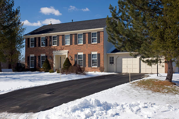 Red Brick Colonial with snow in the winter Classic red brick colonial house in the winter, with snow in the front yard, pine trees, a cleared black top driveway, and a bright, day time blue sky background.  The house is typical of suburban residences in the Northeast United States.  There is ample copy space for text.   driveway stock pictures, royalty-free photos & images