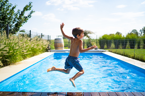 rear view four year old boy jumping into private pool in garden on sunny summer day back view with blurred pool in the background