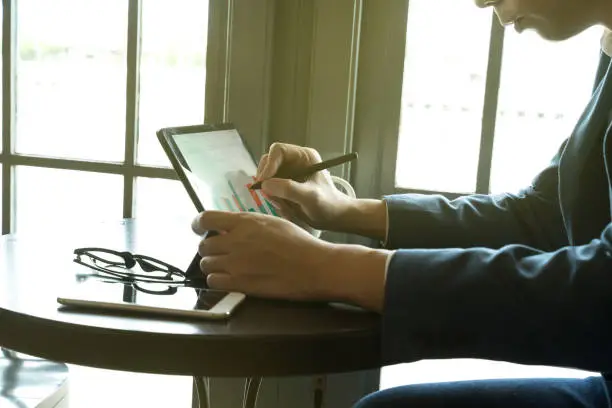 Photo of businessman using  drawing comment in tablet for analysis graph visualization at coffee shop