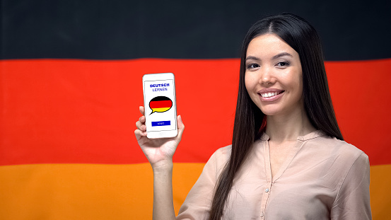 Nice woman holding phone with language study app, German flag on background