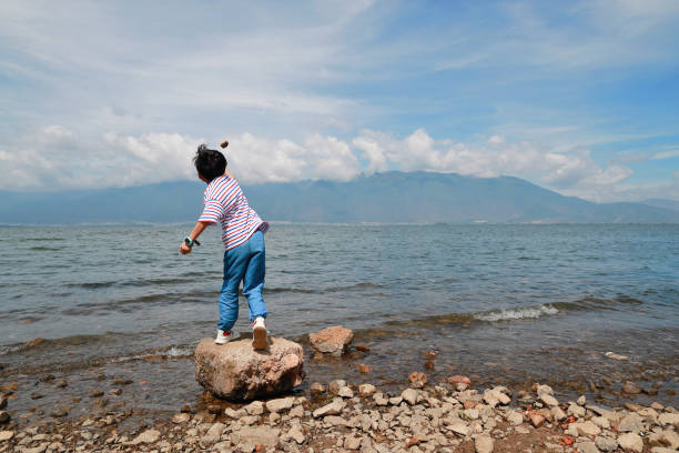 Back view little boy standing and throwing a stones to the river