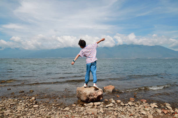 posição traseira do rapaz pequeno que está e que joga pedras ao rio - throwing stone little boys child - fotografias e filmes do acervo