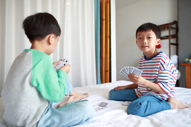 Mid adult father whispering a strategy to his son while playing cards against mother and daughter on a patio.