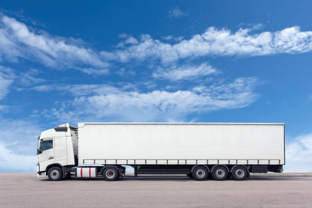A truck with trailer parked on a lot with sky background.