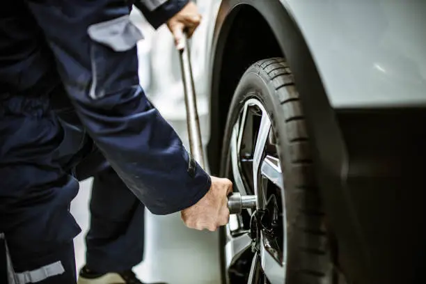 Photo of Close up of a repairman changing wheel and tire in a workshop.