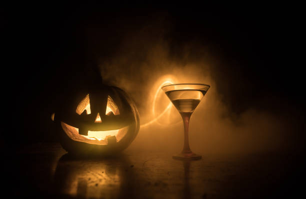 Halloween pumpkin orange cocktails. Festive drink. Halloween party. Funny Pumpkin with a glowing cocktail glass on a dark toned foggy background. stock photo