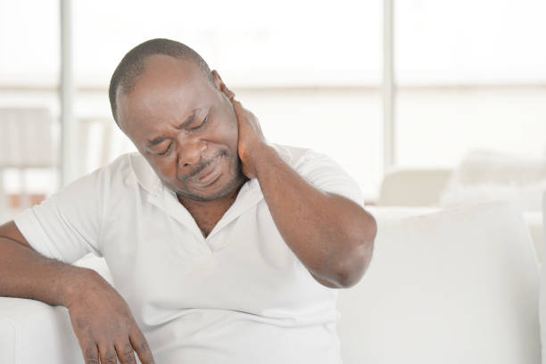 Pain in the neck of a man from fatigue. Tired neck. Elderly african man suffering from neck pain at home on couch. Males sense of fatigue, exhausted, stressed. African man massages her painful neck with her hands. The concept of body and health. black male massage stock pictures, royalty-free photos & images