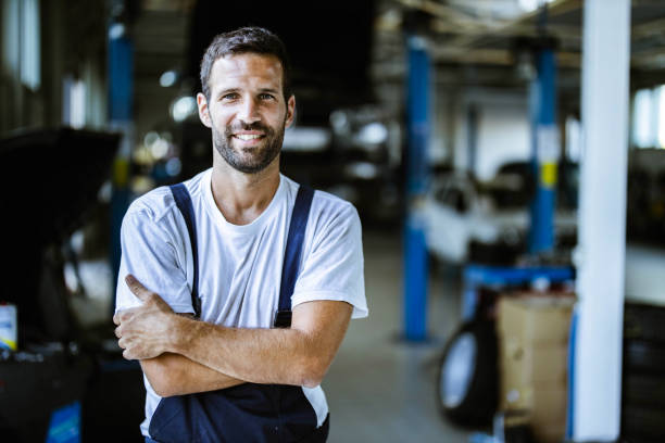 happy mechanic with crossed arms in auto repair shop. - manual worker one person young adult men imagens e fotografias de stock