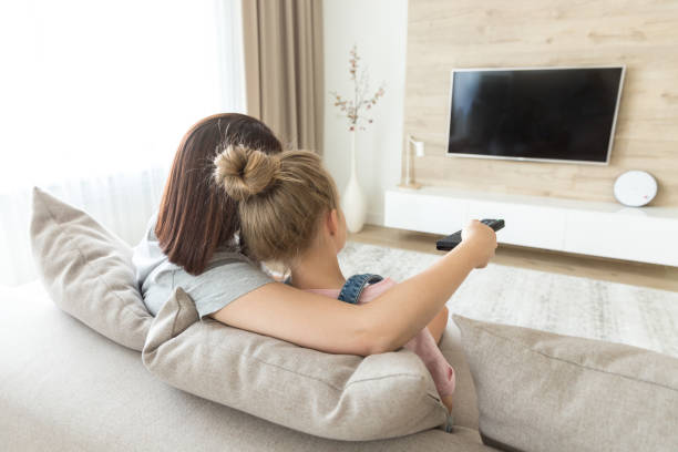 istock Mother and daughter sitting on sofa watching tv 1164678498