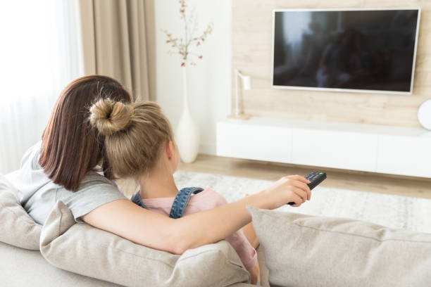 istock Mother and daughter sitting on sofa watching tv 1164678506