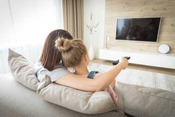 istock Mother and daughter sitting on sofa watching tv 1164678533