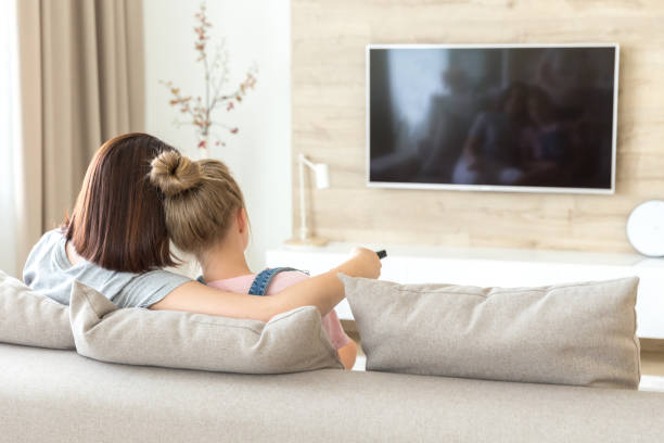 istock Mother and daughter sitting on sofa watching tv 1164678542
