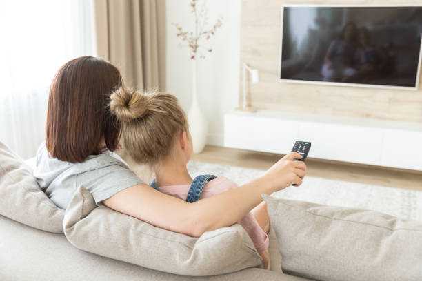 istock Mother and daughter sitting on sofa watching tv 1164678573