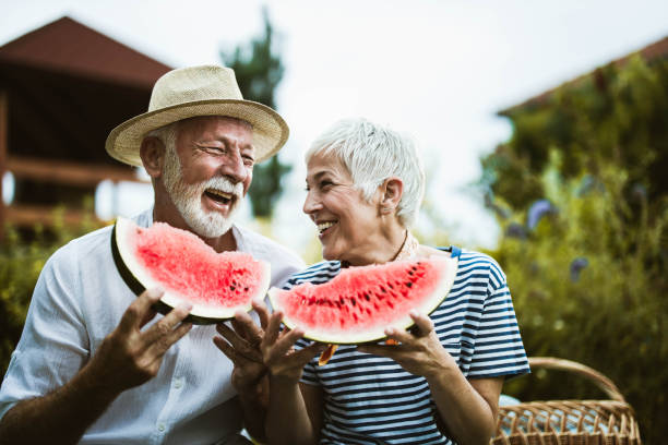 allegra coppia matura che si diverte mentre mangia anguria durante la giornata al sacco nella natura. - picnic watermelon summer food foto e immagini stock