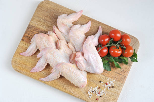 istock Raw chicken wings on a wooden board. The composition is complemented by cherry tomatoes, parsley and spices. View from above. 1164679033