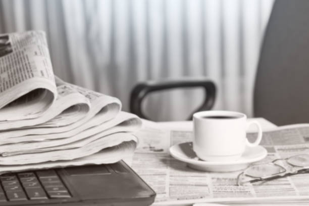 Newspaper on the desk, laptop, cup of coffee.