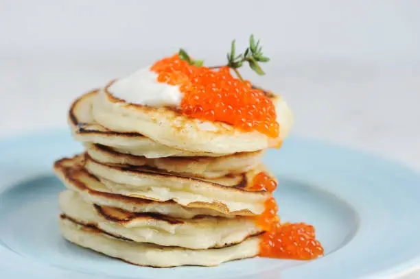 Pancakes with red caviar and sour cream on a plate. Light background. Close-up. Macro shooting. The concept of a festive feast.