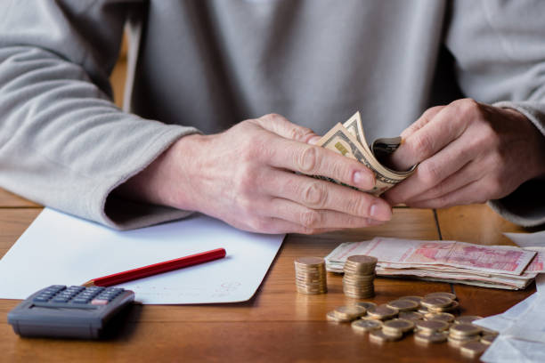 istock Close up man with calculator counting, making notes at home, hand is writes in a notebook. Stacked coins arranged at deesk. Savings finances concept. 1164685284