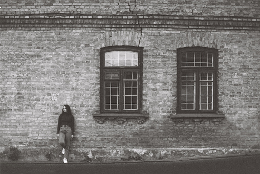 Black and white film photo of young Caucasian  woman standing near old building