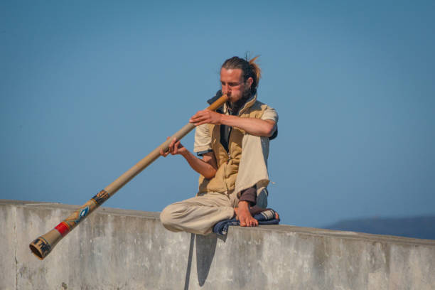 Finisterre, Galicia, Spain, May 2018: man playing didgeridoo on concrete wall with blue sky in background