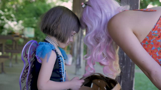 Woman in a pink wig bending over to talk to a young girl wearing fairy wings