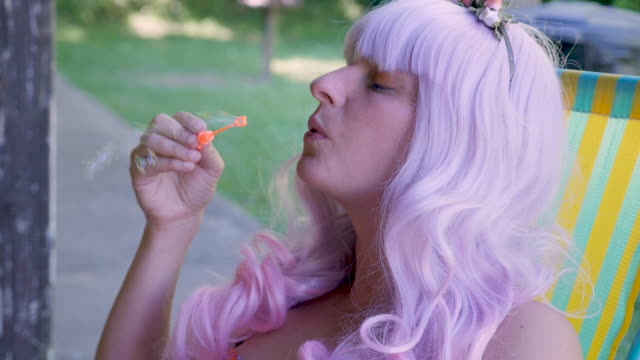 Profile of a woman in a pink wig blowing bubbles in slow motion