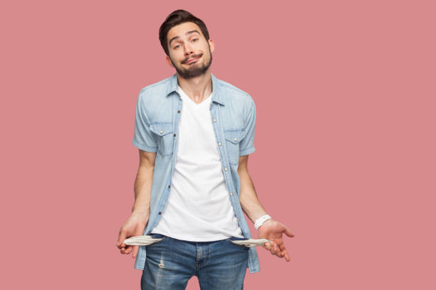 no tengo dinero más. retrato de joven barbudo en bancarrota triste con camisa azul estilo casual de pie y mostrando su bolsillo vacío y mirando a la cámara. - infame fotografías e imágenes de stock