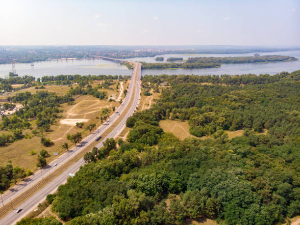 View from the drone to the highway, forest, river with islands and bridge. Wonderful view from the drone to the highway, forest, river with islands, the bridge and the city in the distance. filming point of view highway day road stock pictures, royalty-free photos & images