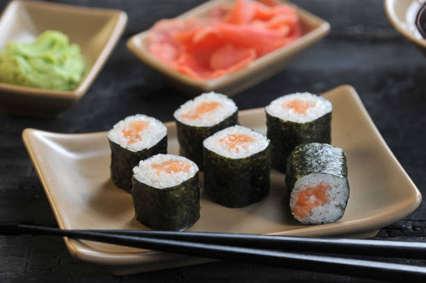 istock Roll with salmon on a light ceramic plate. Next to a plate of chopsticks. Ginger pickled and wasabi in bowls. 1164702886
