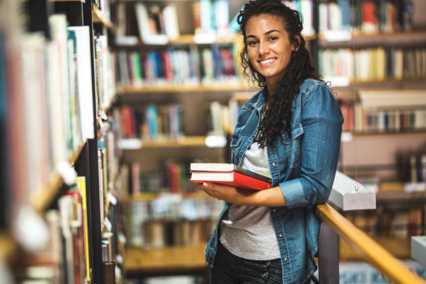 istock Young female student read and learns by the book shelf at the library. 1164704285