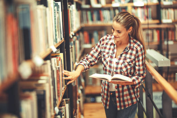 istock Young female student read and learns by the book shelf at the library. 1164704288